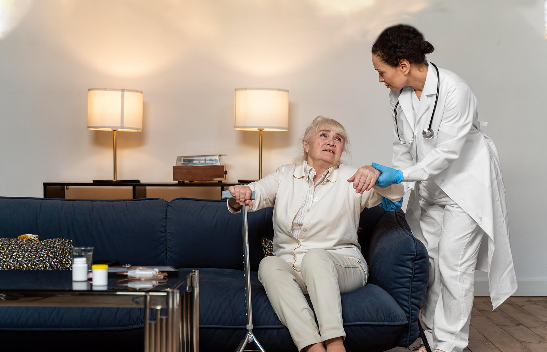 Caregiver helping an older woman up from the sofa at home